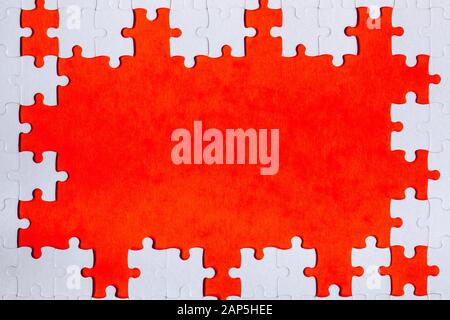 Framing in the form of a rectangle, made of a white jigsaw puzzle. Frame text and jigsaw puzzles. Frame made of jigsaw puzzle pieces on orange backgro Stock Photo