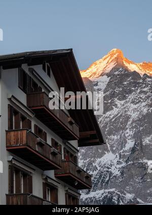 Wetterhorn mountain in background with a rooftop of a local chalet hotel in foreground. Photographed at dusk with the sun reflecting off the summit. Stock Photo