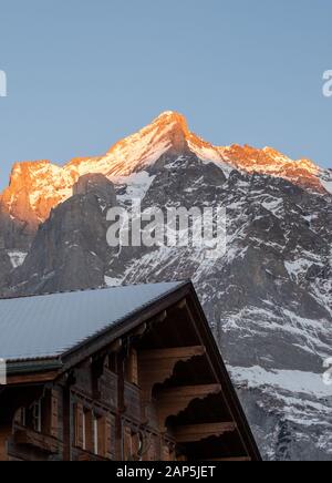 Wetterhorn mountain in background with a rooftop of a local chalet hotel in foreground. Photographed at dusk with the sun reflecting off the summit. Stock Photo