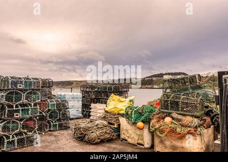 Fisherman’s storage with lobster pots, nets, rope and buoys.  There is a headland in the distance and a cloudy sky above. Stock Photo