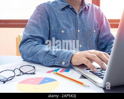 Man wearing blue shirt typing and working with laptop computer on table near the window in office. Stock Photo