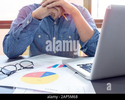 Businessman wearing blue shirt thinking about working with laptop computer on table near the window in office. Stock Photo