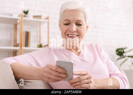 Cheerful senior lady enjoying modern cellphone at home Stock Photo