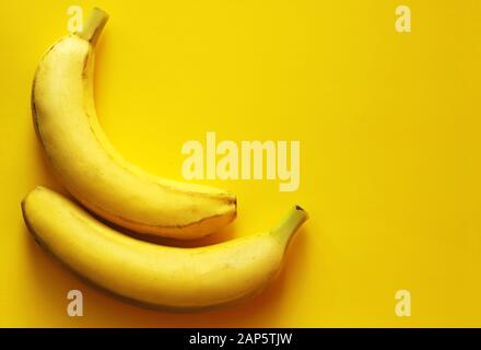 close-up of two ripe bananas lying side by side on a yellow background, top view Stock Photo