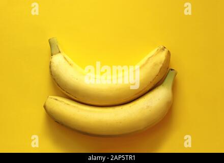 two banans lying in spoon position on a yellow background Stock Photo