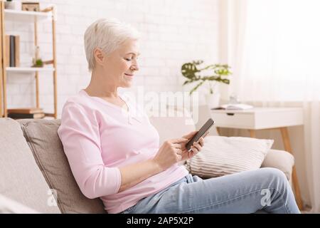 Senior woman chatting on smartphone with friends at home Stock Photo