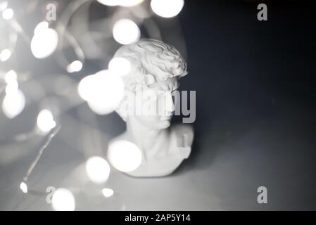 Gypsum statue of David's head. Michelangelo's David statue plaster copy with light garland on grey background. Selective focus Stock Photo