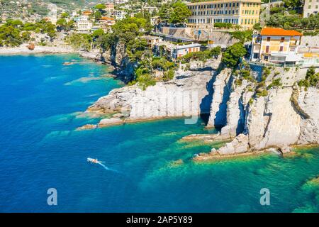 White boat sailing near rocky coast in Camogli, Italy. Aerial view on Adriatic seaside, liguria. Stock Photo