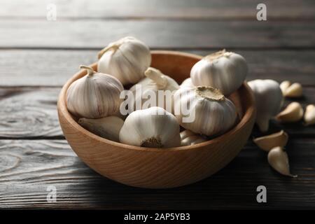 Wooden bowl of fresh garlic bulbs, slices on wooden background, top view. Closeup Stock Photo