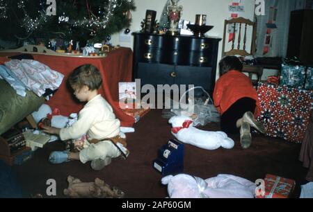 Two children are entirely surrounded by presents, which they unwrap under a Christmas tree in a suburban home on Christmas morning, 1959. () Stock Photo