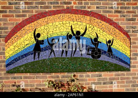 Mosaic on brick wall showing a rainbow effect and a group of  various people Stock Photo