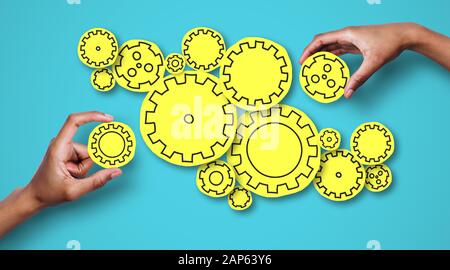 Two hands adding gears to shining mechanism over blue background Stock Photo