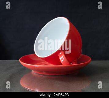 The Red cup lies in saucer on table.Photography with reflection on black background Stock Photo