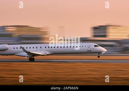 Traffic at airport. Airplane landing on runway against terminal building at golden sunset (blurred motion). Stock Photo