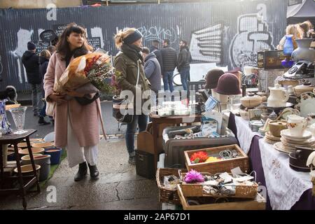LONDON - December 20, 2020 A girl in a faux fur coat walks past a counter with old things sold at a flea market Stock Photo