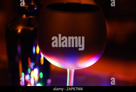 View on isolated black cocktail glass partly illuminated by soft colorful light. Blurred bottle background. Stock Photo
