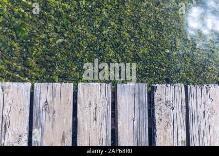 Wooden board empty over sea, can be used for display or present a product. Summer season. Empty perspective wooden planks over the reflection of green Stock Photo
