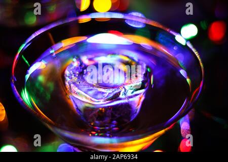 Glass to view on cocktail glass with ice cube in vibrant colors. Colorful bright magic bokeh background. Stock Photo