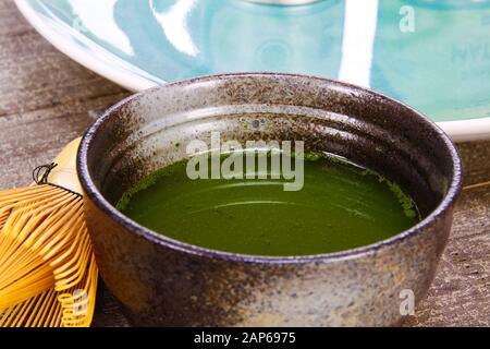 Matcha tea preparation concept: Close up of isolated set for brewing green Matcha tea: one bamboo whisk and scoop, ceramic bowl on old wood table Stock Photo