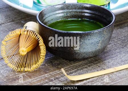 Matcha tea preparation concept: Close up of isolated set for brewing green Matcha tea: one bamboo whisk and scoop, ceramic bowl on old wood table Stock Photo