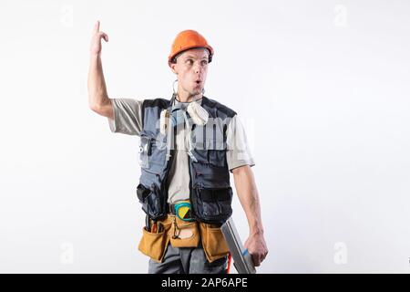 The builder shows up in surprise. In work clothes and hard hat. On a light gray background. Stock Photo