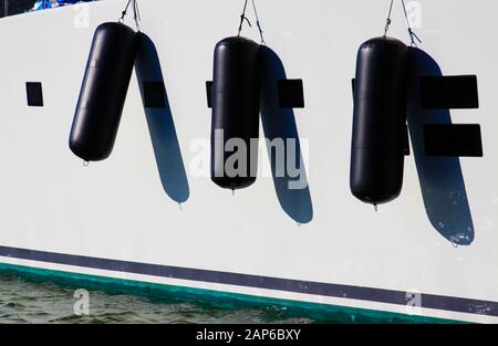 View on white boat side of luxury yacht with three black fenders in natural bright sun light - Marine de Cogolin, France Stock Photo