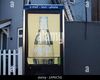 weather worn coca cola advertisement on BT phone box window Stock Photo