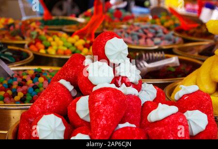 Close up of pile of sweets in shape of strawberry with blurred bowels filled with sweet candies on French market - St. Tropez, France Stock Photo