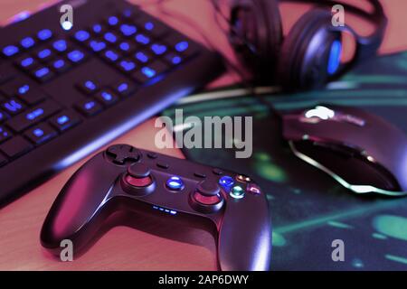 Modern gamepad and gaming mouse lies with keyboard and headphones on table in dark playroom scene close up. Devices for playing video games at home Stock Photo