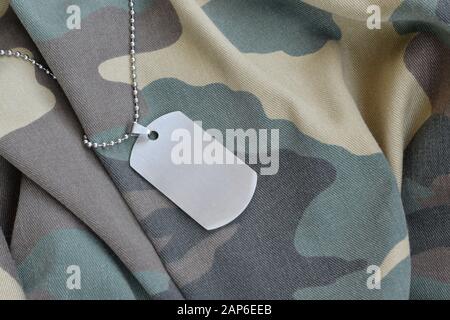 Silvery military beads with dog tag on camouflage fatigue uniform. Army token on soldiers camo jacket rear part Stock Photo