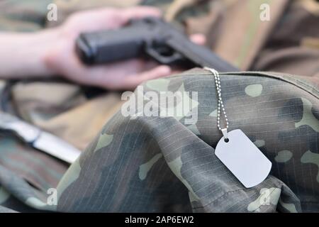 Dog tag with armed hand of dead recruit of Russian army lies on many camouflage clothes. Killed in action or suicide concept Stock Photo