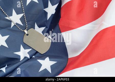 Silvery military beads with dog tag on United States fabric flag. Army token on USA banner close up. Veterans day concept Stock Photo