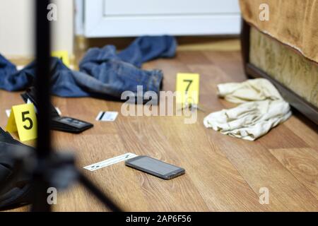 Crime scene investigation - numbering of evidences after the murder in the apartment. Broken smartphone, wallet and clothes with evidence markers clos Stock Photo