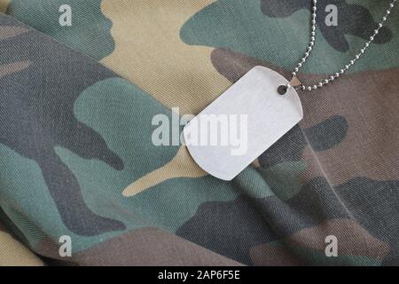 Silvery military beads with dog tag on camouflage fatigue uniform. Army token on soldiers camo jacket rear part Stock Photo