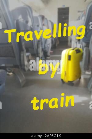 The inscription TRAVELLING BY TRAIN on the background of the interior of the train car with a yellow suitcase Stock Photo