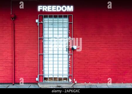 Red Wall with Door secured by Iron Gratings and the Word Freedom in Neon Letters Stock Photo