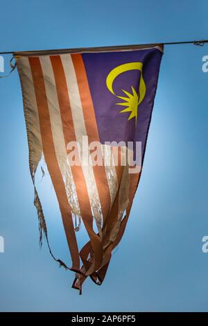 Worn out Malaysian Flag flying with sun shining through Stock Photo