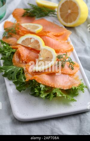 Slices of smoked salmon with lettuce and sliced lemon on a cutting board Stock Photo
