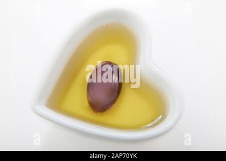 heart shaped bowl on a white background with dark olive in olive oil