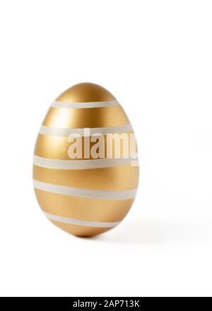 Golden colored easter egg isolated on white background. Modern easter egg painted in a fashion golden color. Happy Easter time. Stock Photo