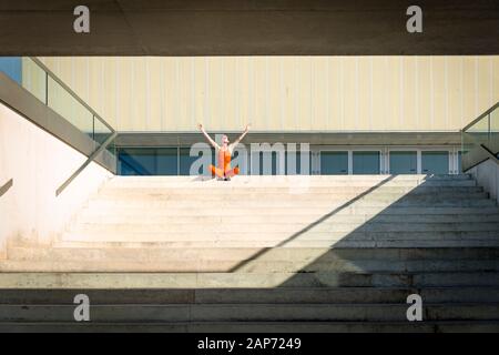 sporty woman sitting on top step with her arms raised in success Stock Photo