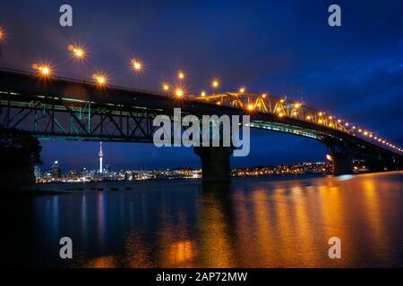 Looking over Waitemata Harbour at downtown Auckland city from the North Shore at night with the Harbour Bridge in foreground. New Zealand. Stock Photo