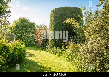 Early morning light in a quiet corner of an English garden in mid-Spring showing evergreen and deciduous trees and a broad grass path Stock Photo