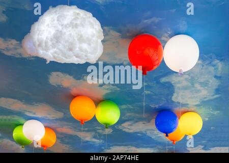 Fragment of a ceiling stylized as a vault of heaven with lamps in the form of clouds and balloons close-up. Stock Photo