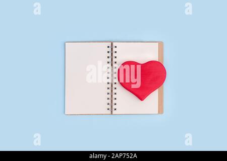 Red wooden love heart on open notebook on blue background. Valentine's day concept, copy space. Stock Photo