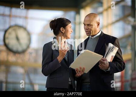 Two business colleagues having a discussion while standing inside a station. Stock Photo