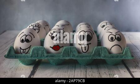 White eggs with faces painted in the shell on a cyan blue cardboard Stock Photo