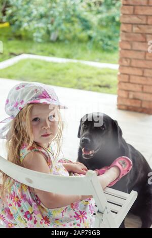Girl sitting in the yard with a big black dog Stock Photo