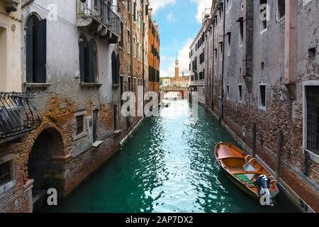 Tourists cross a bridge over a residential canal with the cathedral of San Giorgio Maggiore bell tower in view across the grand canal in Venice Italy Stock Photo