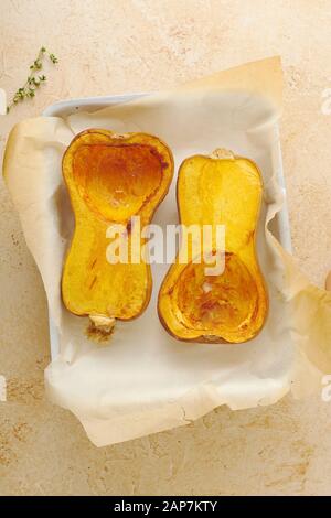 Roasted halves of seeded butternut squash with olive oil, salt and thyme on baking tray covered with parchment paper Stock Photo